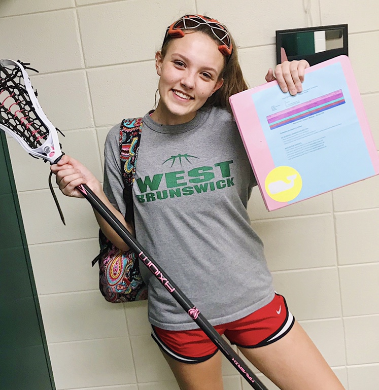 Sophomore Lacrosse Player, Elizabeth Norfleet poses for the camera with her lacrosse equipment and binder.