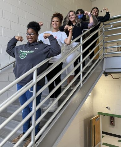 Female students and staff flex on the stairs.