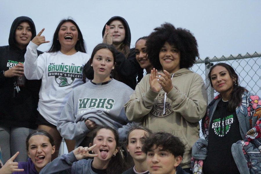 The womens varsity soccer team in the stands supporting and cheering on the womens softball team.