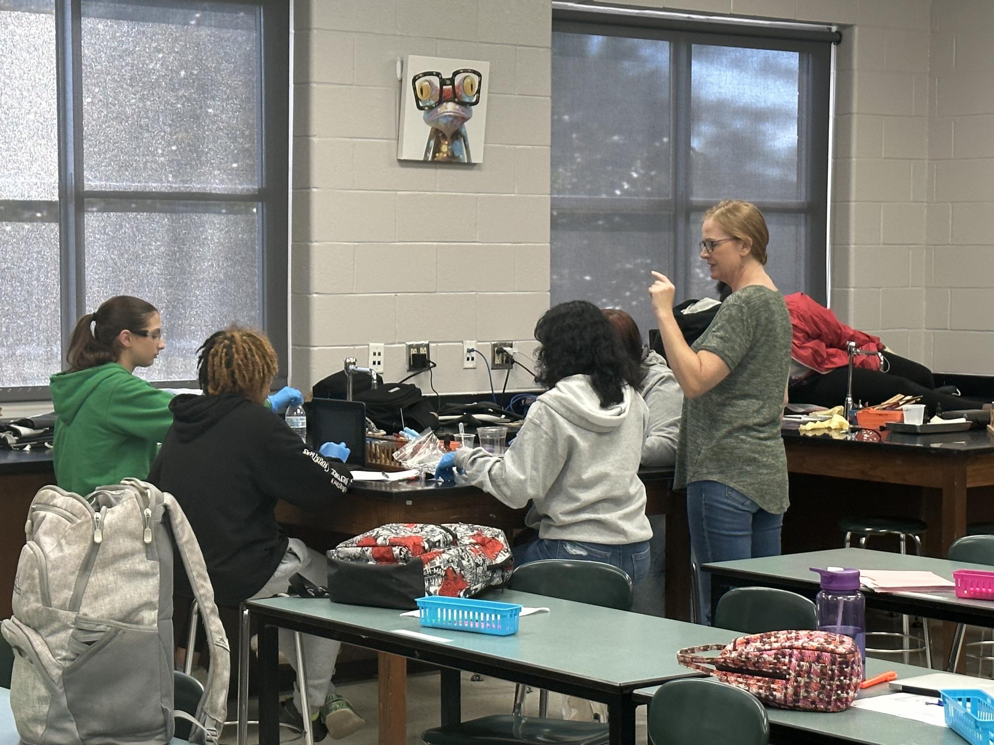 Teacher, Ms. Jones is helping a group of kids with the lab. She is getting them started so that they can figure out who the kidnapper is. 