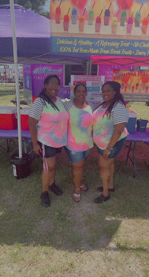 (From left to right) AhYanna Jackson, Roberta Jackson, and Annaca Jackson stand posing with one another in front of AhYannas Italian Ice trailer. 