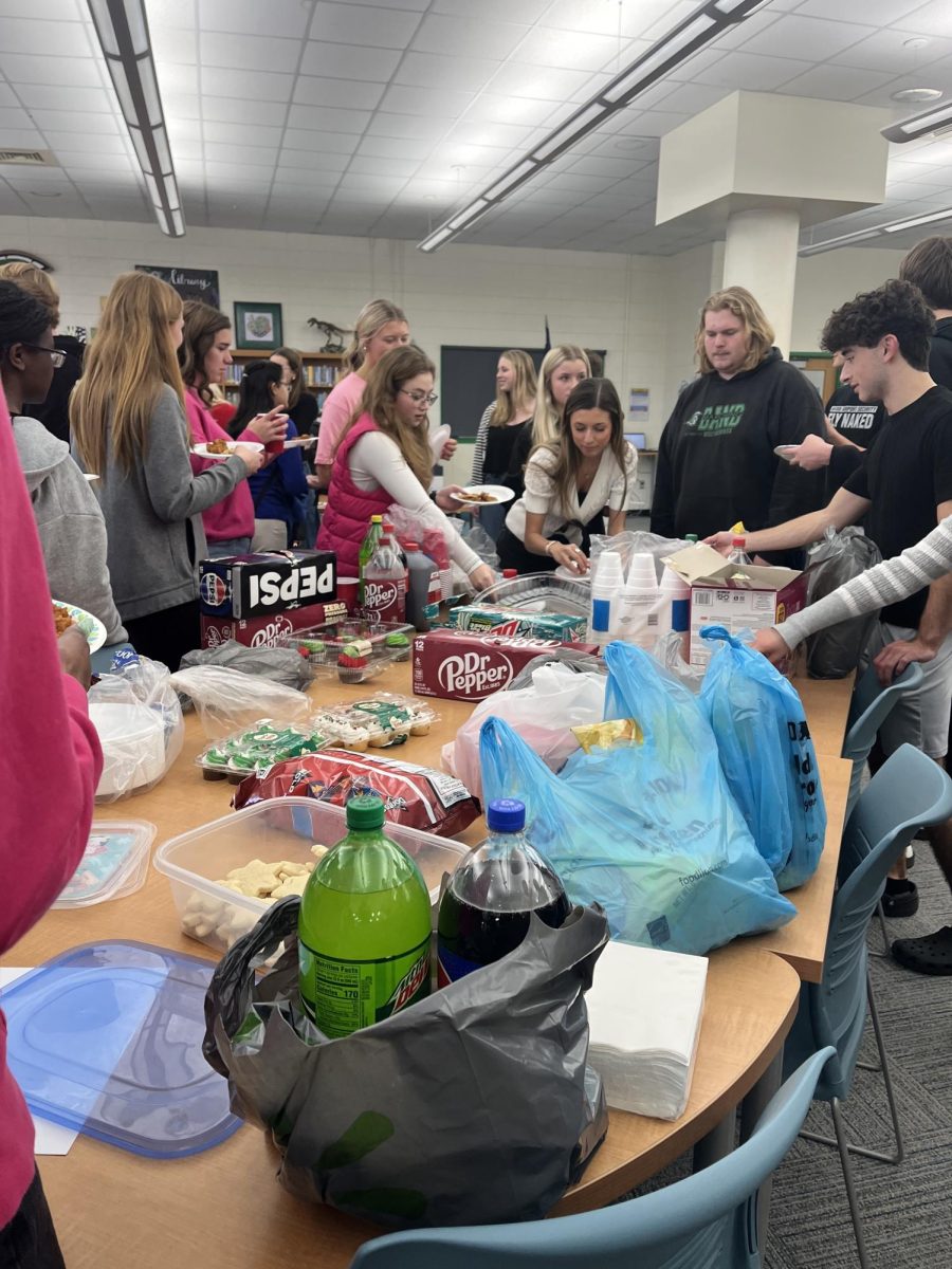 Members surround a table with food brought from fellow NHS students. They reach for different foods to put onto their plates. 