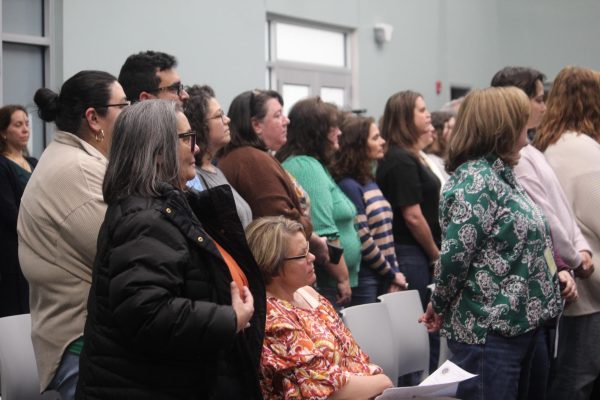 Teachers from across the county stand up in support of the speech that teacher Kourtney Saavedra presents to the board. 