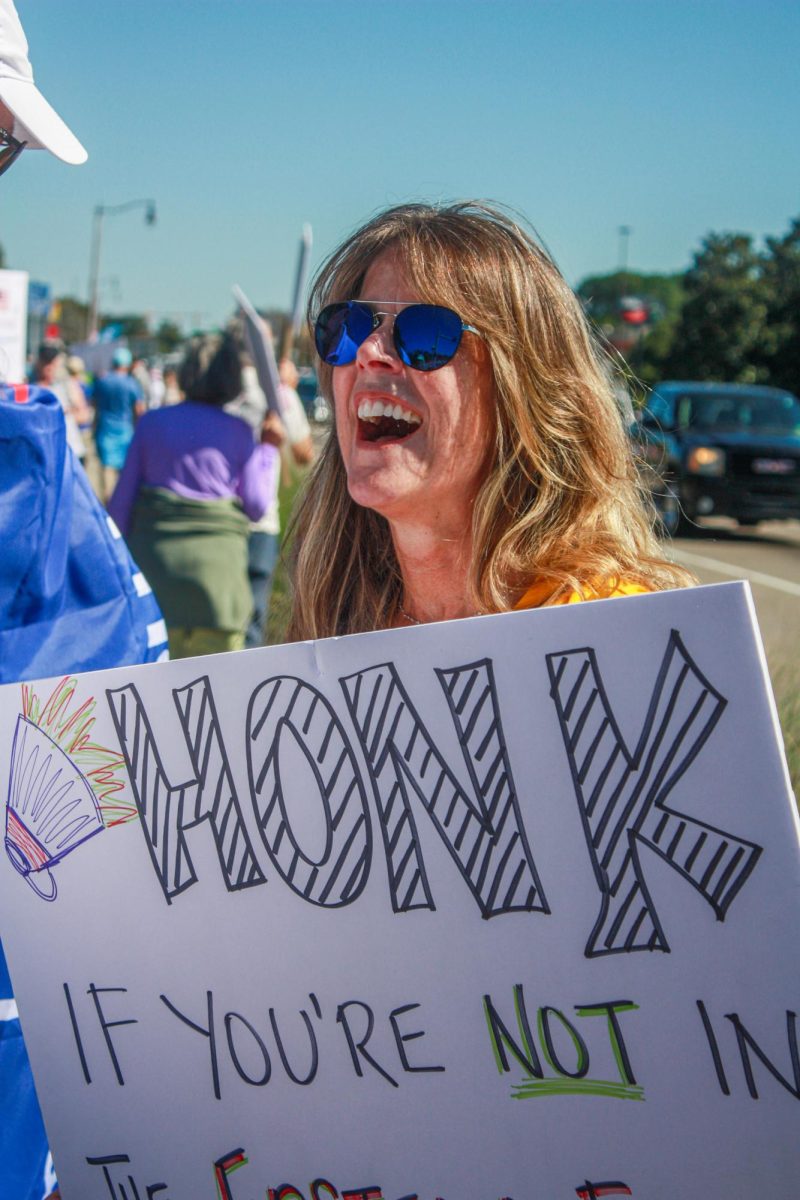 A protester laughing to a new friend about her sign that reads, "Honk if you're not in Epstein files.”
