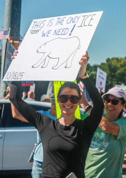 A woman walks across the street during the No Kings Protest with a sign stating the only kind of ice she wants is the kind for polar bears.